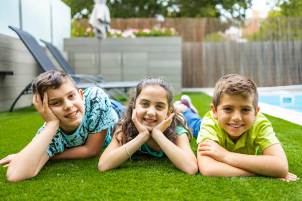 Synthetic grass cleaning as three children rest on artificial grass by the pool
